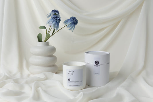 White candle labeled 'Quiet Time' and a white container on a draped white fabric background
