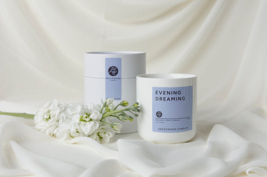 Candle labeled 'Evening Dreaming' with a matching container on a white fabric background