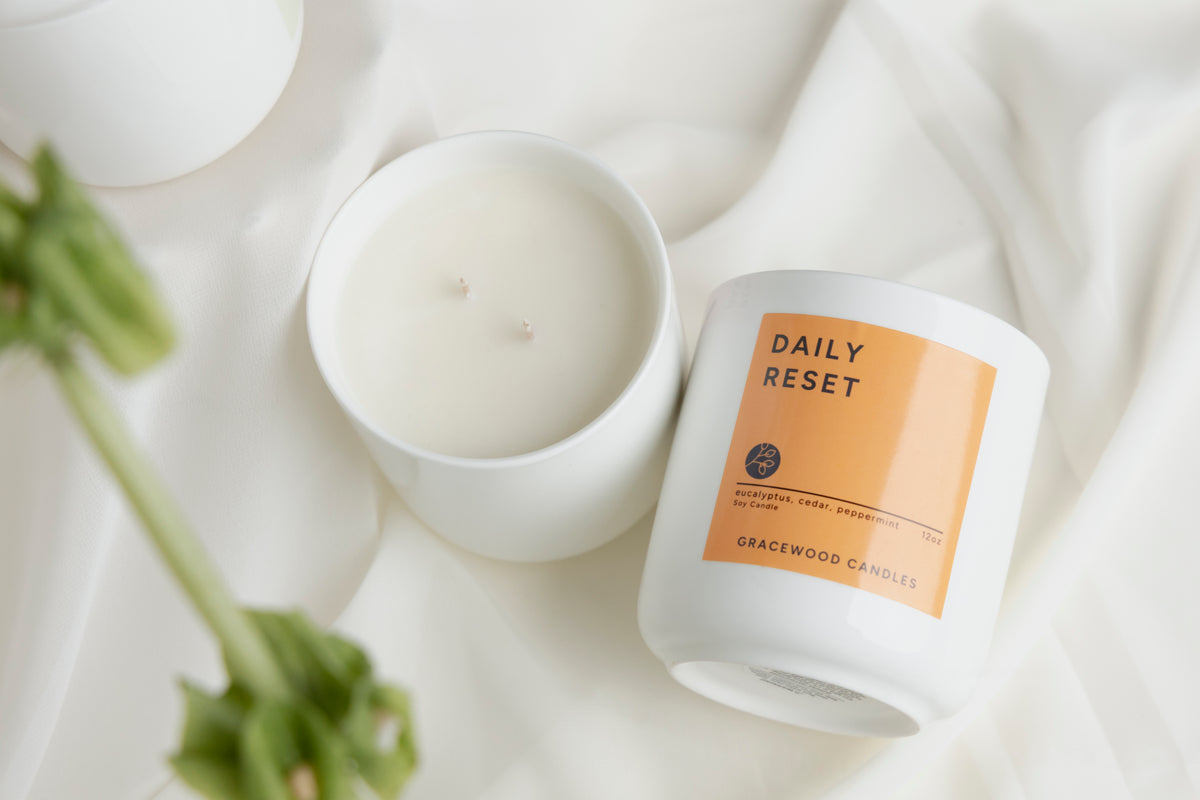 Candle labeled 'Daily Reset' on a white surface with a plant.