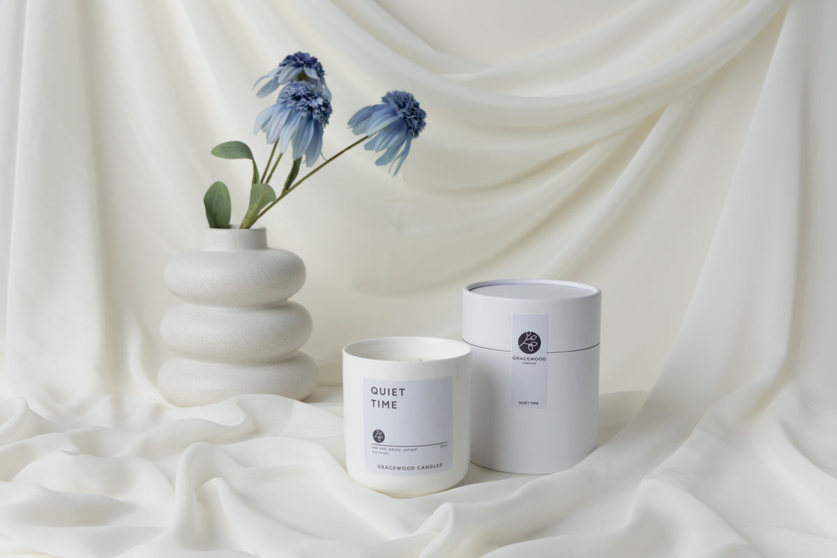 White candle labeled 'Quiet Time' and a white container on a draped white fabric background