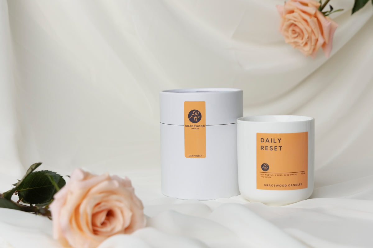 Candle and packaging with 'Daily Reset' text on a white background with roses.