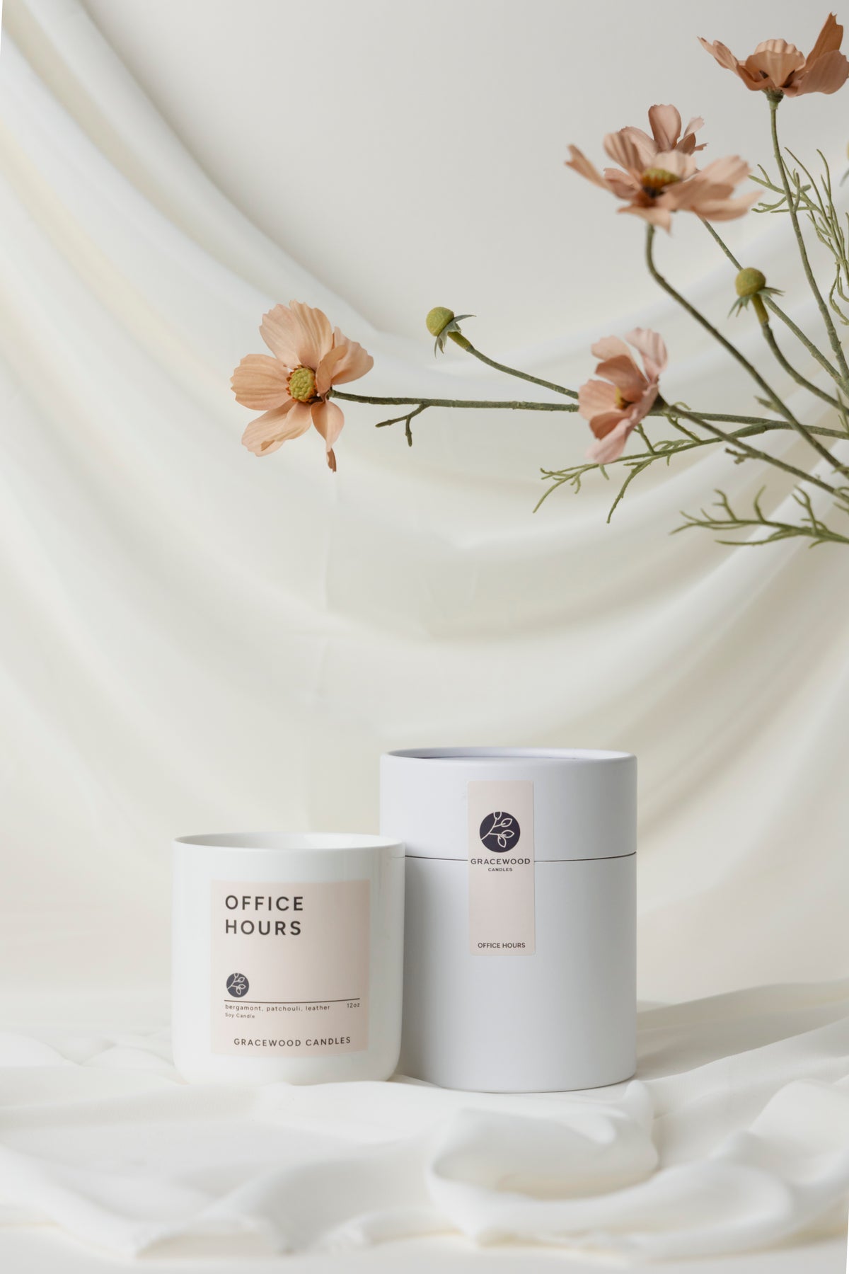 Two candles with labels on a white fabric background with flowers.