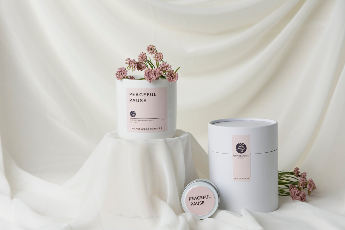 Candle labeled 'Peaceful Pause' with flowers on a white fabric background