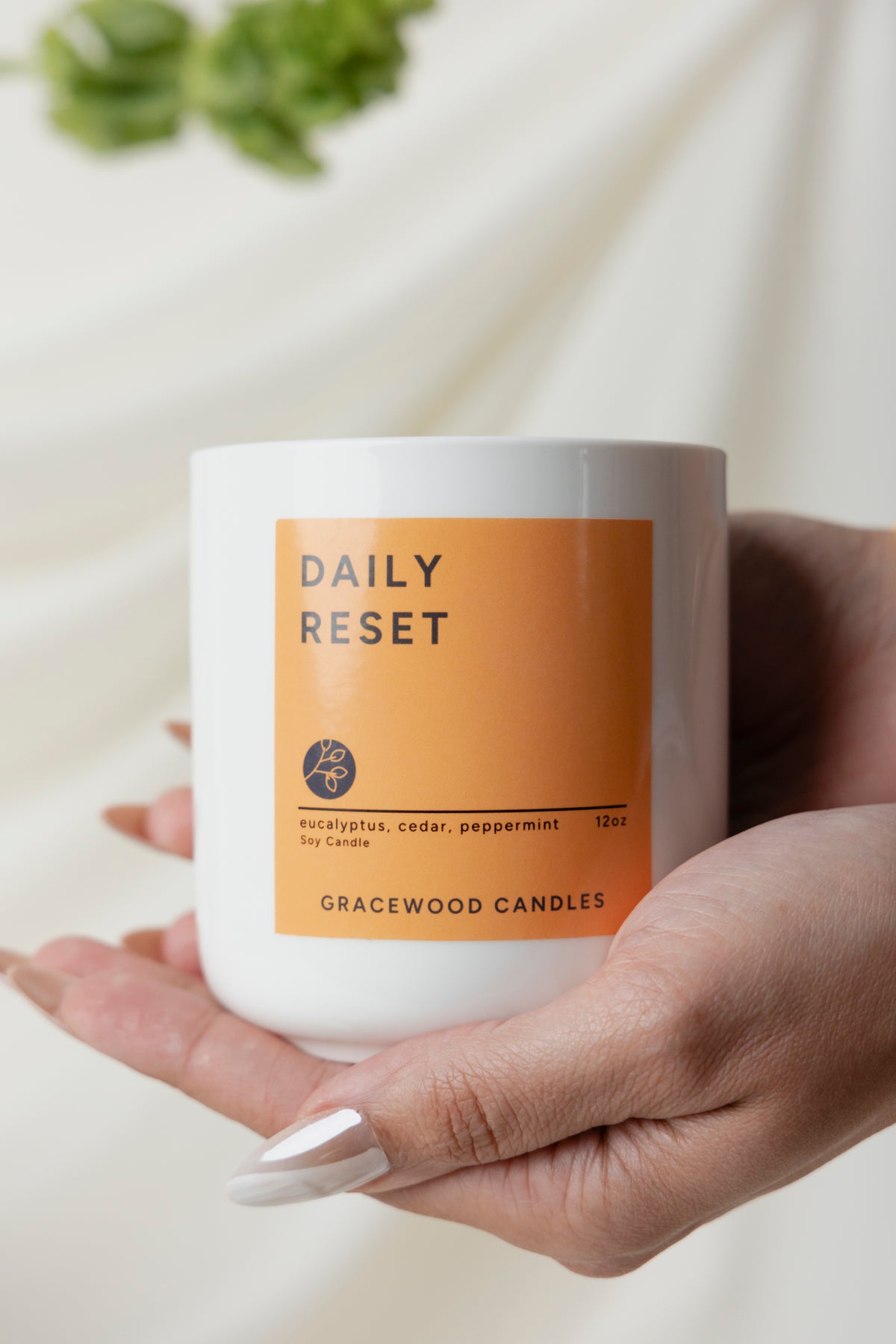 Hand holding a candle labeled 'Daily Reset' by Gracewood Candles on a neutral background
