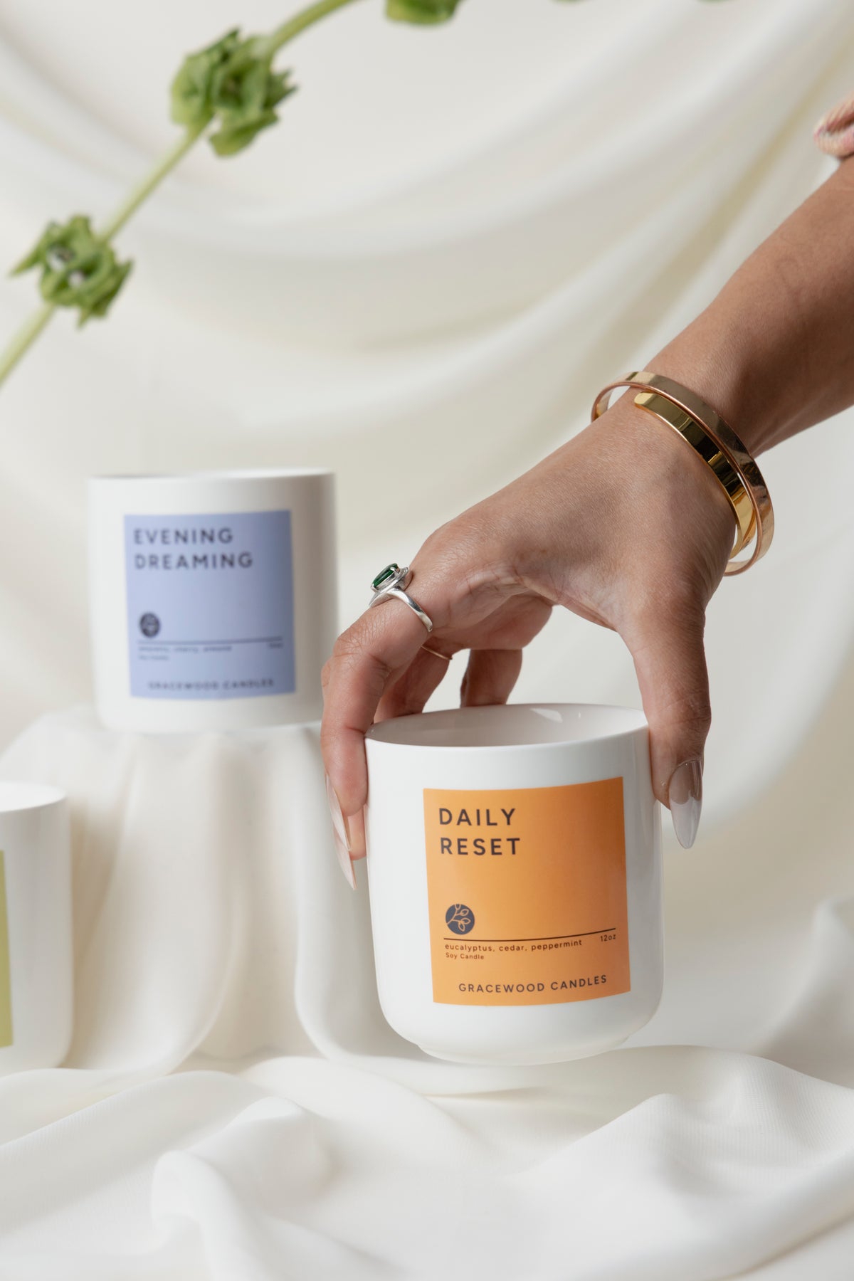Person holding a candle labeled 'Daily Reset' with another candle labeled 'Evening Dreaming' in the background.