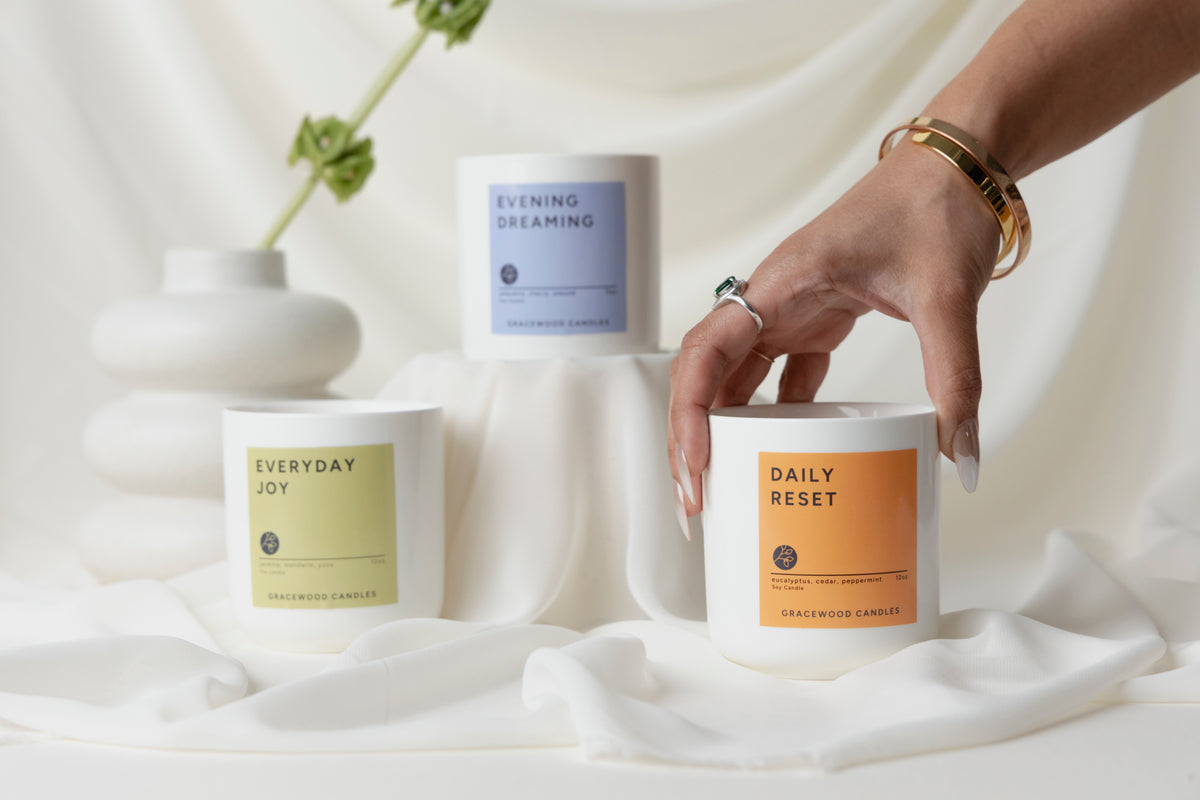 Candles with labels 'Everyday Joy', 'Evening Dreaming', and 'Daily Reset' on a white fabric background.