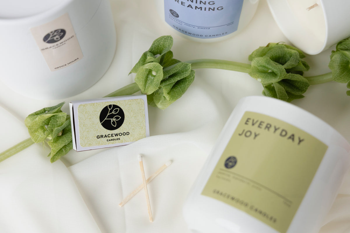 Candles with labels on a white surface with greenery